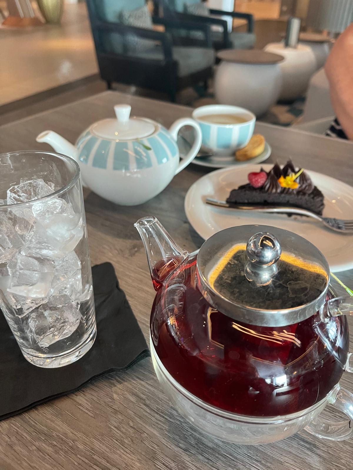 Afternoon tea served on a ship: a glass teapot, a cup and a small plate of cake on a dark table