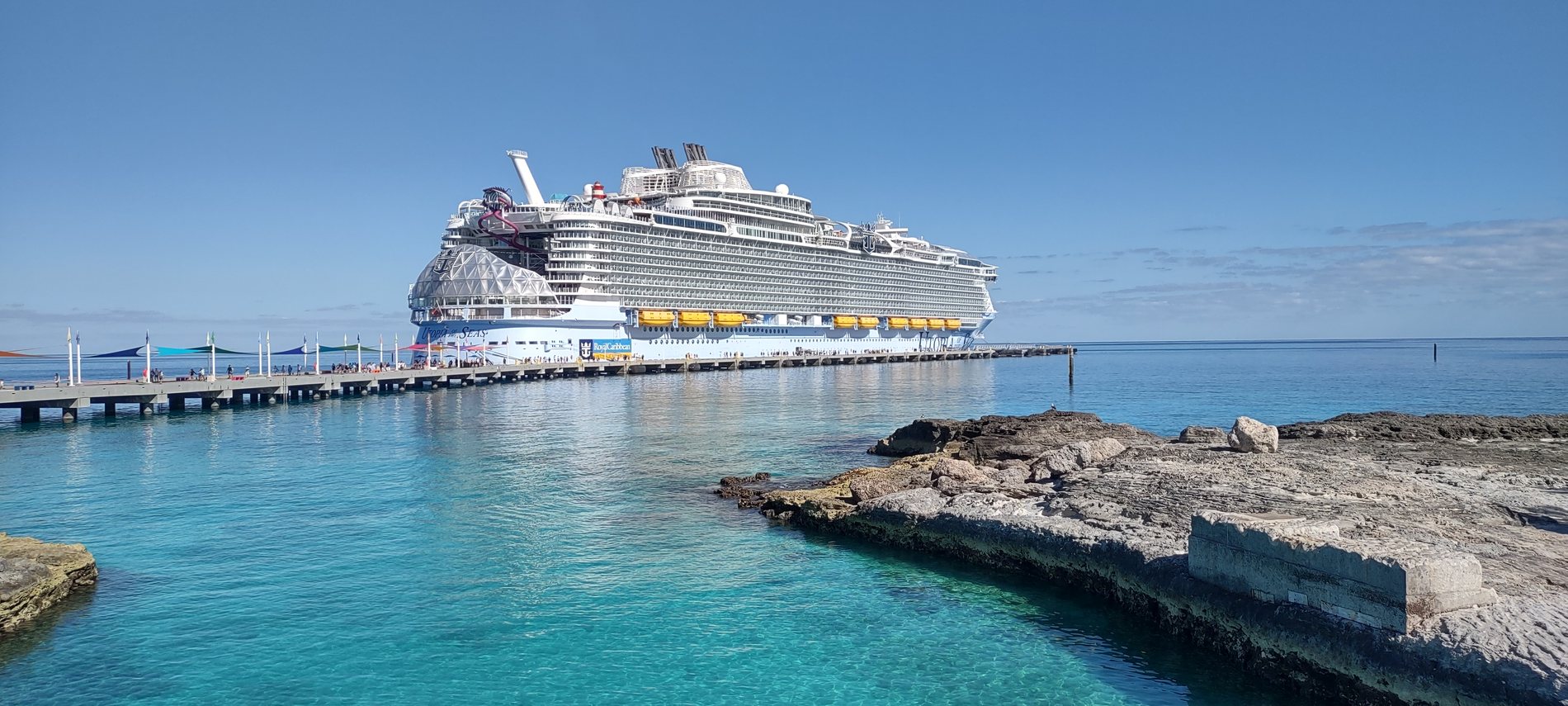 A large cruise ship berthed alongside the pier at Perfect Day at CocoCay, turquoise water in the foreground