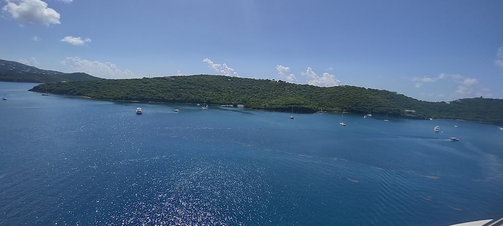 The green hills and anchorage of St. Thomas seen from a cruise ship, yachts moored in deep blue water